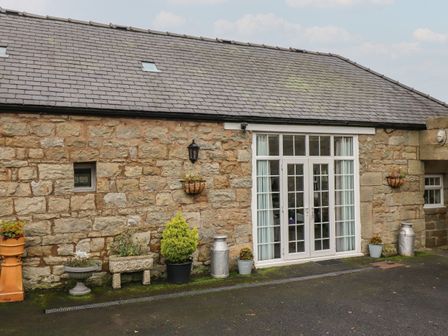 A stone building exterior with white double doors and various potted plants at The Barn in Middleton near Ponteland