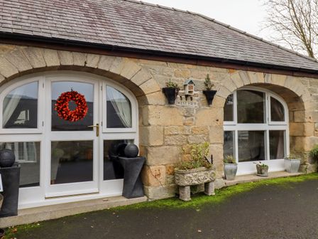 Stone building with arched windows and door with a red wreath and plants outside at West View Middleton near Ponteland