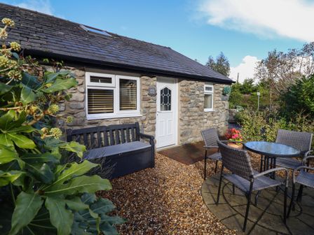An outdoor seating area with a stone building a white door windows a black bench and a round glass table with four chairs at Tan Isa in Harlech
