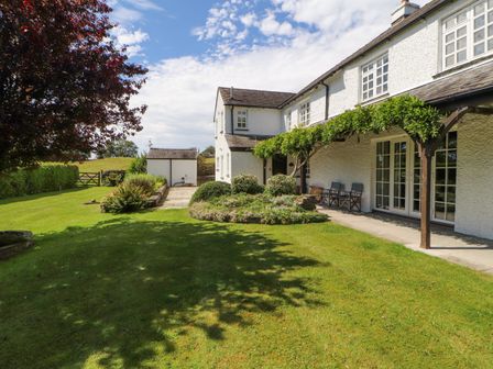 A garden with lawn shrubs and patio furniture outside a white house at Stang Farm in Kendal