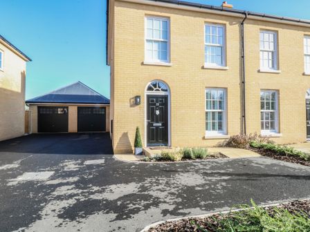 A front view of a yellow brick semi detached house with a black door and four windows beside two black garages at The Hollies in Norwich
