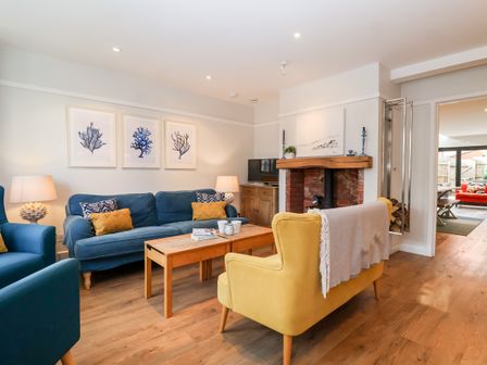 A living room with blue and yellow chairs a wooden coffee table and a fireplace at Fawcett Cottage in Aldeburgh