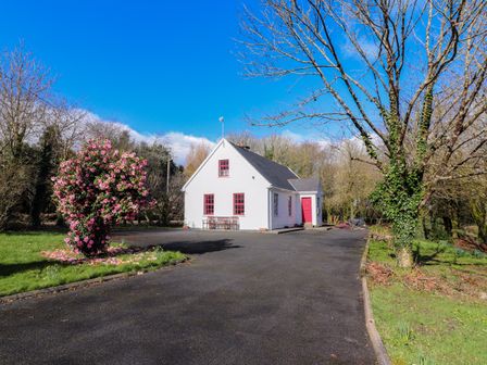 A white house with red doors and windows surrounded by trees and a flowering bush at Kyleatunna Cottage in Ennis County Clare