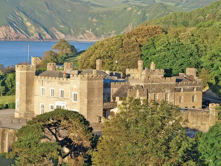 A castle with towers near water and greenery at Watermouth Castle, West Tower Apartment Ilfracombe