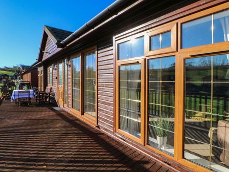 A wooden deck with outdoor furniture and table near a log cabin with large windows at The Fairhaven in Tunstall near Catterick North Yorkshire