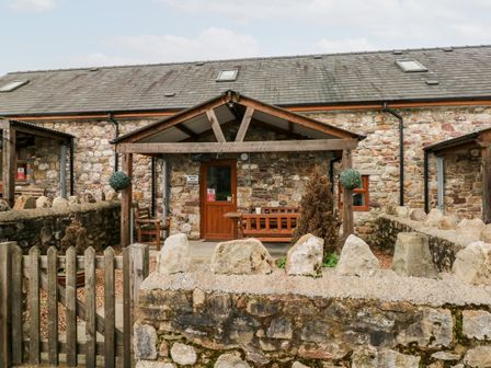A stone cottage with wooden benches and a small garden area at Barn 2 in Ystradgynlais