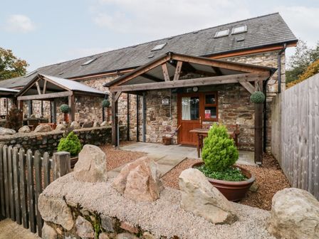 Stone cottage with wooden porch and small garden area with potted plant at Barn 3 Cwm-twrch Isaf near Ystradgynlais