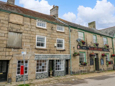 A street view of stone buildings with windows and flower pots hanging outside at The Old Post Office in Praze-An-Beeble