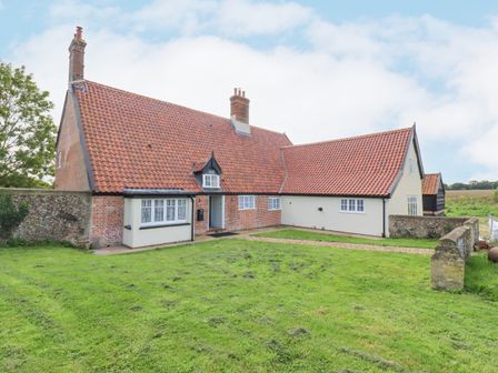 A brick and stucco house with red tiled roofs and chimneys on a grass lawn at West House Farm in Leiston