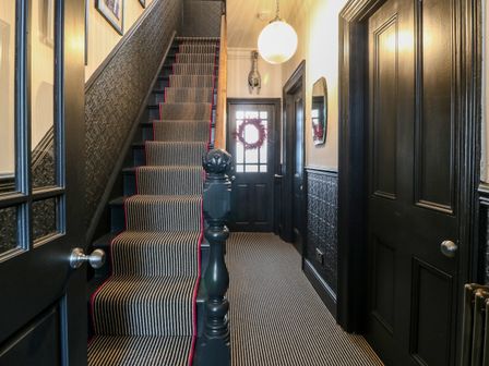 A hallway with a striped carpeted staircase and black doors at Trigfa in Criccieth