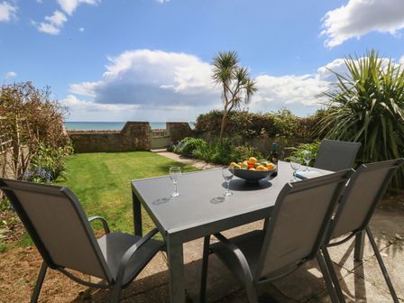 An outdoor patio with a table and chairs overlooking a garden and sea at Blue Yonder in Weymouth