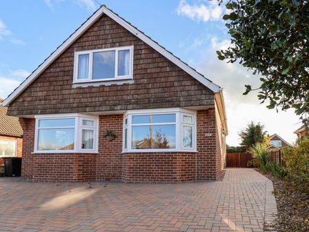 A brick house with two large front windows and a paved driveway with plants on the side at Meadowfields in Whitby