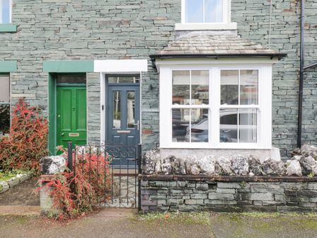 The front of a stone house with a blue door and white framed window next to a small garden with red berries and a black metal gate at Forty Five in Keswick