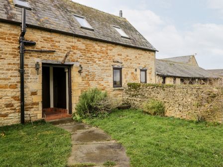 Exterior view of a stone cottage with a tiled roof two skylights and a stone pathway in a grassy yard at Stable Cottage in Moreton-In-Marsh