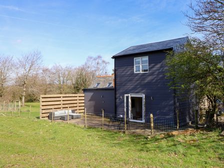 A two-story dark blue house with outdoor seating on a fenced grass lawn at The Stables in Tafarn-Y-Gelyn