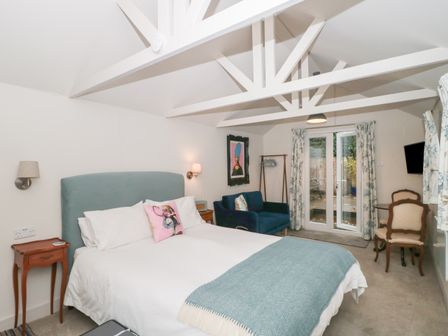 A bedroom with a bed a blue headboard a blue sofa chairs and a small table at The Potting Shed in Combe near Langport
