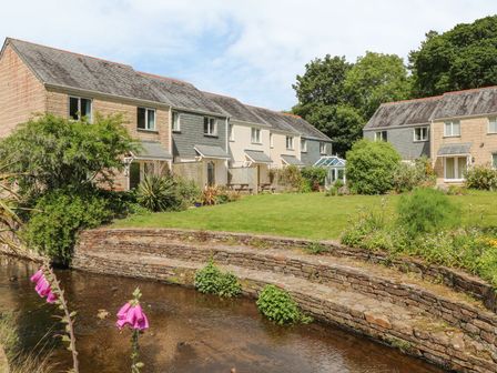A row of houses with gardens behind a stone wall overlooking a shallow stream at Manuka in Falmouth