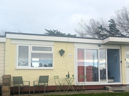 A small patio area with green metal chairs and a table with a bottle and glasses outside a yellow house with a sliding glass door at Culver View in Sandown