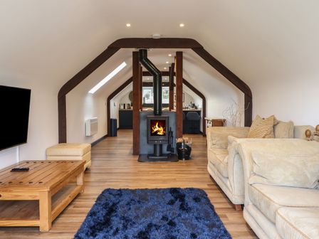 A living room with a wood stove in the center and a beige sofa at Bryn Eglwys Cottage in Llanegryn near Tywyn