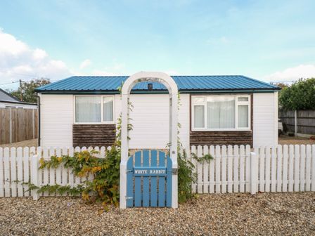 A small house with a blue roof behind a white picket fence and a blue gate with an arch at White Rabbit Cross Lane in Eccles-On-Sea