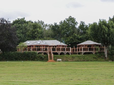 A log cabin with a wooden deck and stairs surrounded by trees and grass at Copper Lodge in Chulmleigh