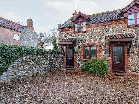 Exterior view of two stone cottages with wooden doors and windows and a gravel driveway at 1 Crowlands Cottages in Holt