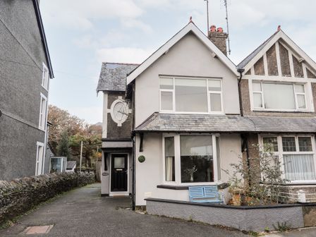 The exterior of a semi detached house with black door a blue bench and a driveway to the side at Gweldon Topsail in Borth-y-Gest near Porthmadog
