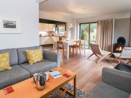 A living room with gray sofas yellow cushions wooden coffee table and a dining area with a table and chairs at Mundays Orford