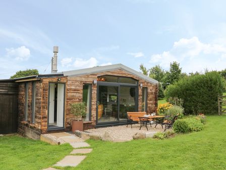 A small wooden cabin with glass doors and windows with outdoor seating and a garden at Windy Willows in Okehampton