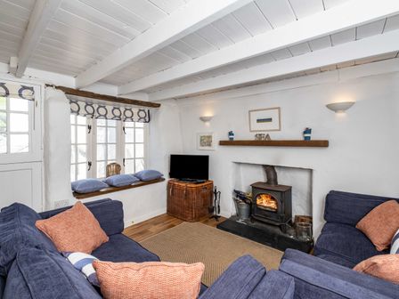 A living room with blue sofas orange cushions a woodburner and a television on a wicker stand at Sea Horses in Port Isaac
