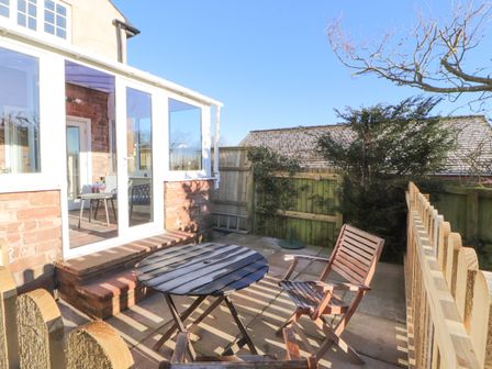 A small patio area with a round table and two wooden chairs by a glass door at Hillside Hideaway in Wigton