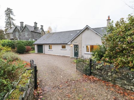 A driveway with gravel leading to a single-story house with green door and windows surrounded by greenery at Tandarra Keswick