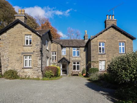 A stone house with multiple windows and chimneys surrounded by plants and gravel driveway at 2 Birkhead Troutbeck near Windermere