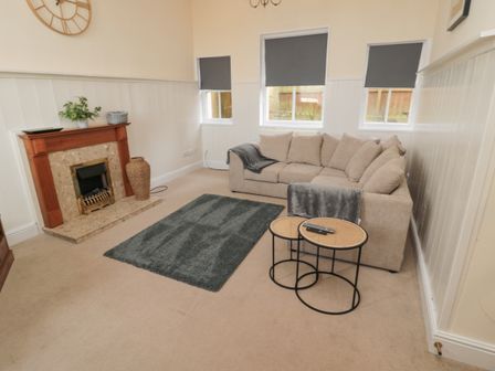 A living room with a beige sectional sofa gray rug and a fireplace at Courtyard Cottage in Alnwick