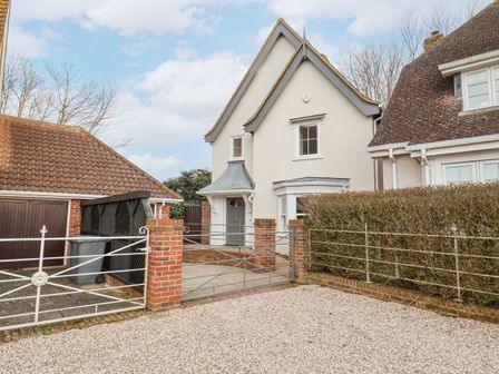 The front of a detached house with a gray door a gravel driveway a metal gate and a garage at 9 Church Farm Rise in Aldeburgh