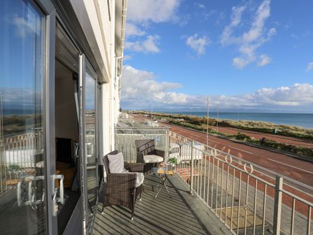 A balcony with two wicker chairs and a small table overlooking a road and the sea at 21 Min Y Mor in Pwllheli