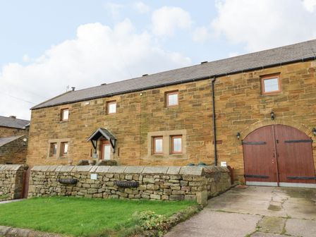 A stone building with multiple windows and a wooden door behind a low stone wall at Winding Wheel Cottage in Cambois near Ashington