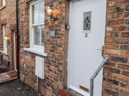 Exterior view of a brick cottage with a white door numbered 2 a window and outdoor light at Jacks Cottage in Keswick