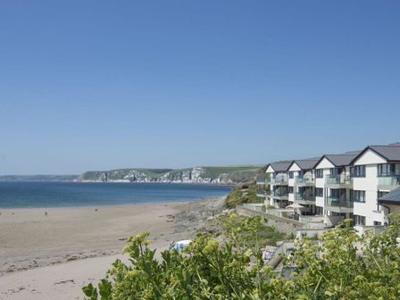 A beach with a row of modern buildings along the shore and cliffs in the background at 19 Burgh Island Causeway Bigbury-On-Sea