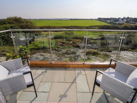 A patio with two chairs and a potted plant overlooking fields and houses at Corrie Knowe in Trearddur Bay