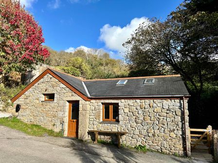 A stone cottage with a wooden door and windows surrounded by trees at Harveys House in Helston