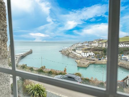 A harbor with buildings on a hill and a car on a road viewed through a window at Chy Lowen in Porthleven