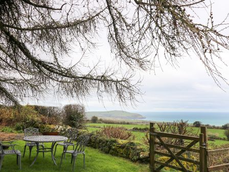 An outdoor garden area with a metal table and four chairs overlooking a grassy field and the sea at Parc y Marriage in Newport Pembrokeshire