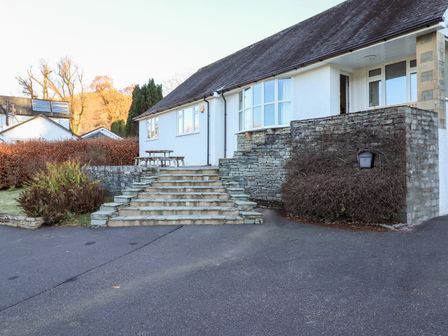 An exterior view of a house with stone steps leading to a patio with a wooden picnic table at Rainbow End in Grasmere