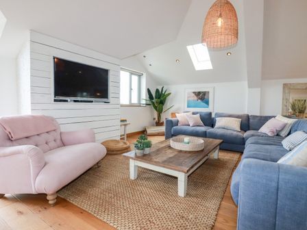 A living room with a pink armchair a blue sectional sofa wooden coffee table and a mounted television at Sea View House in Crantock