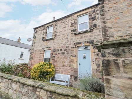 Stone house with blue door and bench outside surrounded by plants at The Haven in North Sunderland near Seahouses