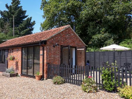 A brick building with a tiled roof and black fence around a patio with table and umbrella at The Grain Store in Haddiscoe