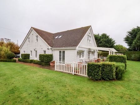 A white house with a tiled roof and a deck with outdoor furniture surrounded by green grass and bushes at Lampland House in Walberswick