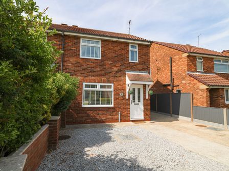 A brick house with a white door and windows with shutters a paved driveway and green bushes at The Whyte Retreat in Hornsea