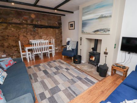 A living room with blue sofas a wood burning stove a dining table with white chairs and a stone wall at Seascape Cottage in Seahouses